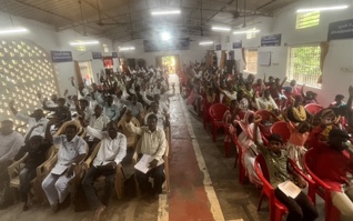 A full congregation seated in a church hall with hands raised