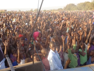 A vast outdoor festival crowd with hands raised in worship