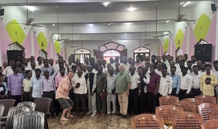 A large group of pastors gathered for a conference photo inside a church hall