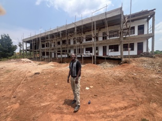 A man standing before a multi-story school building under construction with wooden scaffolding