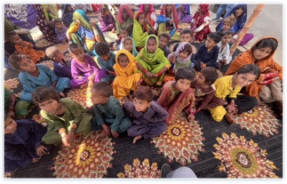 Women and children in brightly colored clothing seated together on patterned mats